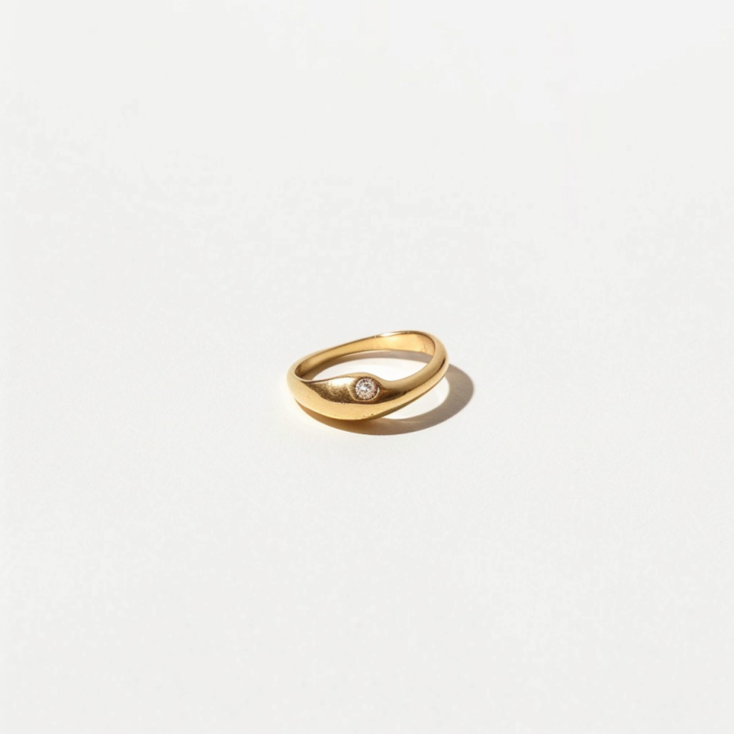 Minimalist gold ring with a smooth curved design and subtle stone detail on a white background